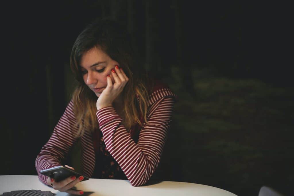 A girl sitting at a table looking at her phone, checking the WhatsApp online status of a contact.