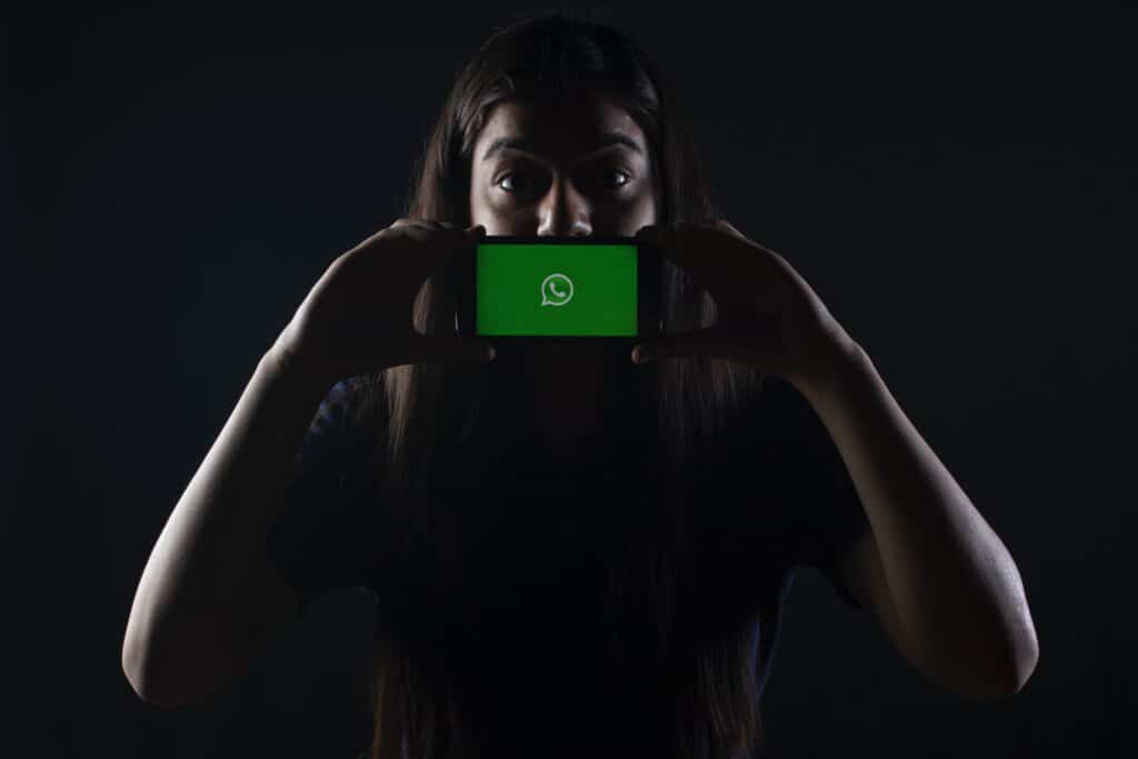 A woman is taking a picture of her phone with a green WhatsApp chat logo on it.