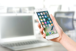 A woman's hand holding an iPhone with a Complete Guide to WhatsApp Remote Sales Strategy displayed on its screen in front of a laptop.