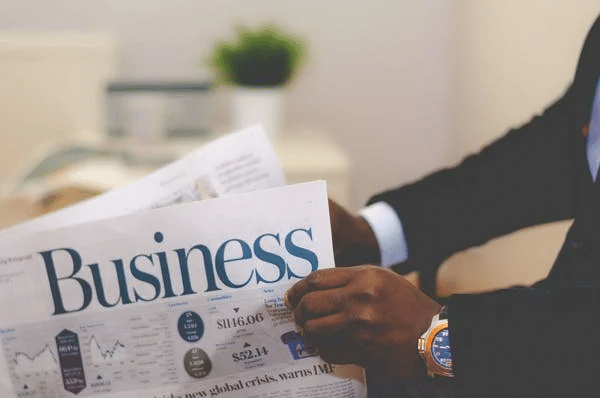 A businessman monitoring WhatsApp activity while reading a newspaper with the word business on it.